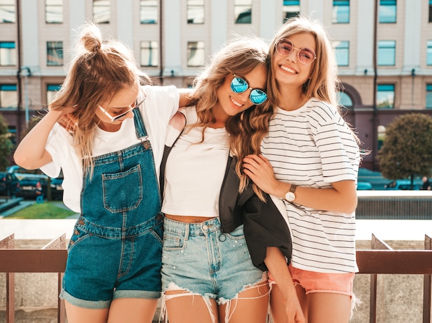 Ritratto di tre giovani belle ragazze sorridenti hipster in abiti estivi alla moda. Donne spensierate sexy in posa sulla strada. Modelli positivi che si divertono in occhiali da sole