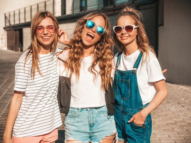 Ritratto di tre giovani belle ragazze sorridenti hipster in abiti estivi alla moda. Donne spensierate sexy in posa sulla strada. Modelli positivi che si divertono in occhiali da sole