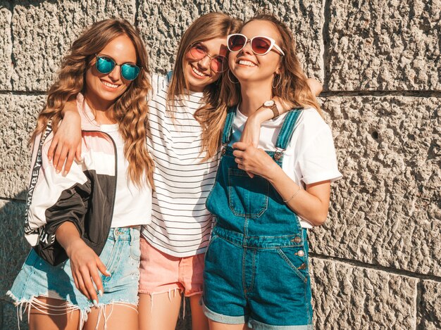 Ritratto di tre giovani belle ragazze sorridenti hipster in abiti estivi alla moda. Donne spensierate sexy in posa sulla strada. Modelli positivi che si divertono in occhiali da sole