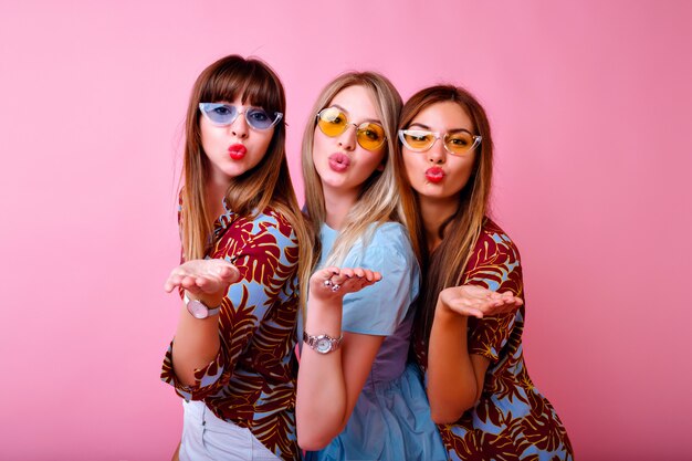ritratto di tre ragazze dei migliori amici super eccitate, vibrazioni positive beate, vestiti e accessori alla moda con stampa tropicale luminosa estiva, muro rosa, sorelle che si divertono.