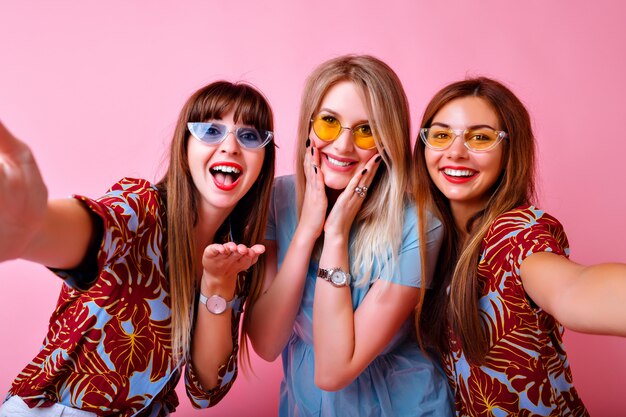 ritratto di tre ragazze dei migliori amici super eccitate, vibrazioni positive beate, vestiti e accessori alla moda con stampa tropicale luminosa estiva, muro rosa, sorelle che si divertono.