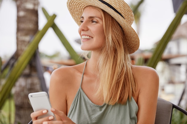 Ritratto di turista femminile rilassato riposa nell'interiore del caffè con il telefono cellulare