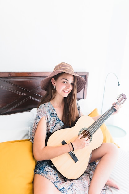 Ritratto di un adolescente felice che si siede sul letto a suonare la chitarra
