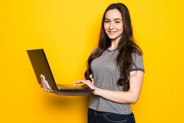 Ritratto di un adolescente sorridente che tiene il computer portatile isolato su una parete gialla