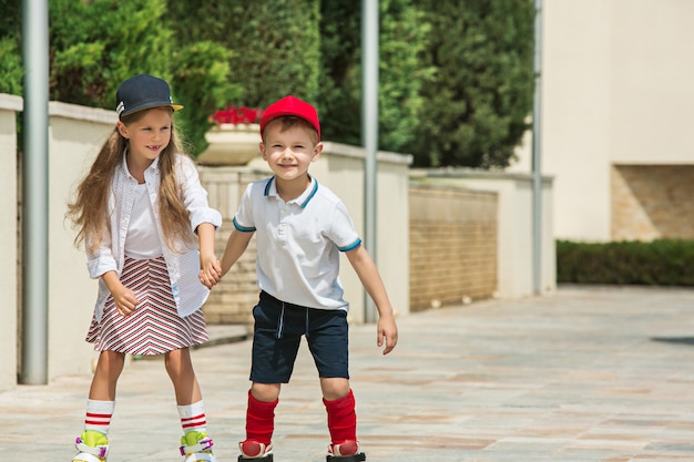 Ritratto di un'affascinante coppia di adolescenti che pattinano insieme sui pattini a rotelle al parco. Ragazzo e ragazza caucasici teenager. Bambini vestiti colorati, stile di vita, concetti di colori alla moda.