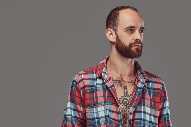 Ritratto di un bel hipster tatuato alla moda con una barba ben tagliata in una camicia di flanella, in posa in uno studio. Isolato su un grigio.