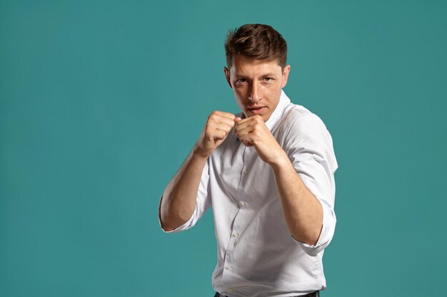 Ritratto di un bell'uomo bruno con occhi marroni, che indossa una classica camicia bianca. Si comporta come se stesse combattendo mentre posa in uno studio su uno sfondo blu. Concetto di gesticolazione e s