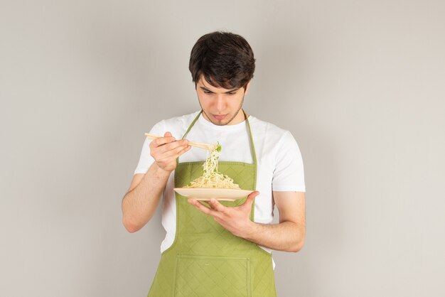 Ritratto di un bell'uomo modello in grembiule che tiene un piatto con il cibo.