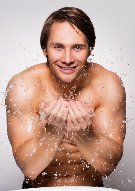 Ritratto di un bell'uomo sorridente che si lava il viso sano con acqua sul muro grigio.