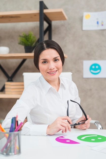 Ritratto di un bello psicologo femminile sorridente che tiene gli occhiali neri a disposizione