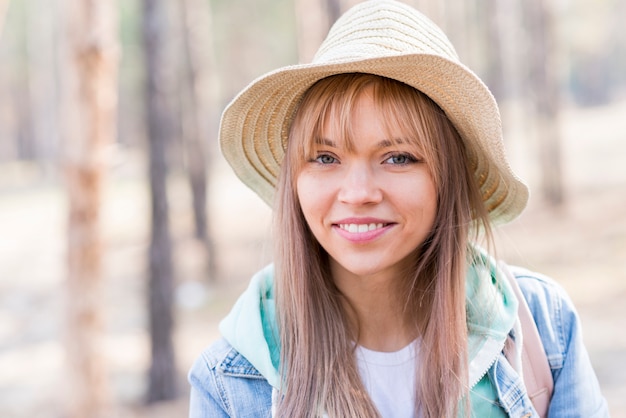 Ritratto di un cappello da portare turistico femminile giovane sorridente che esamina macchina fotografica