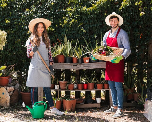 Ritratto di un giardiniere femminile e maschio che tiene zappa e cestino di piante in vaso nel giardino