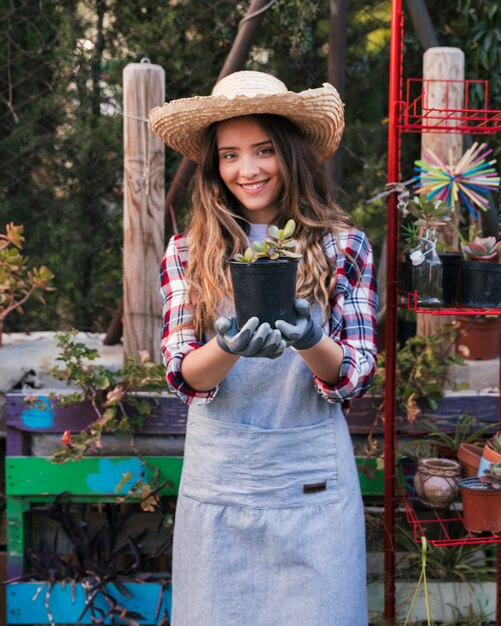 Ritratto di un giardiniere femminile sorridente che porta cappello che mostra la pianta del cactus nel giardino