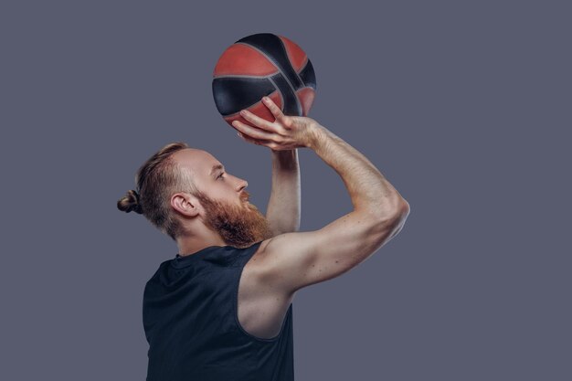 Ritratto di un giocatore di basket rosso in un abbigliamento sportivo nero che tiene una palla con le mani sopra la testa, isolato su sfondo scuro testurizzato.