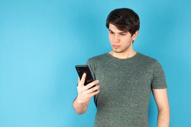 Ritratto di un giovane che utilizza un telefono cellulare contro il blu.