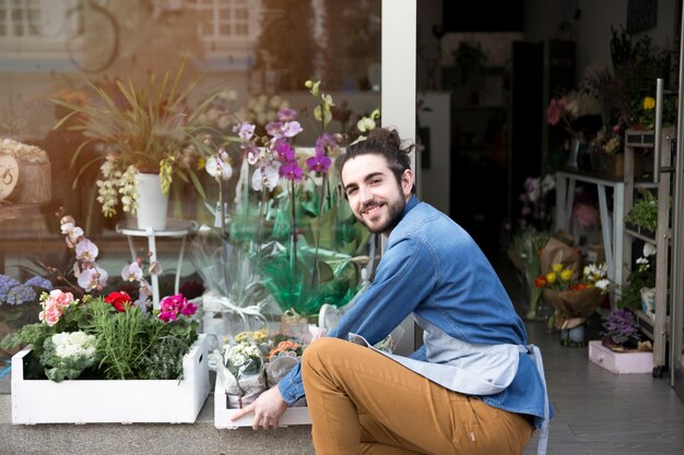 Ritratto di un giovane fiorista maschio sorridente che organizza i fiori nella cassa