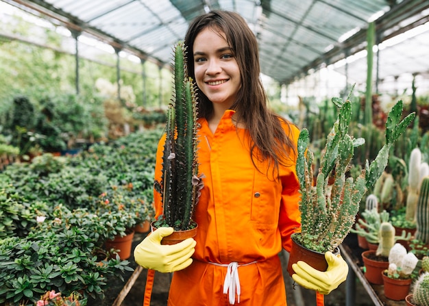 Ritratto di un giovane giardiniere femminile sorridente che tiene le piante in vaso del cactus