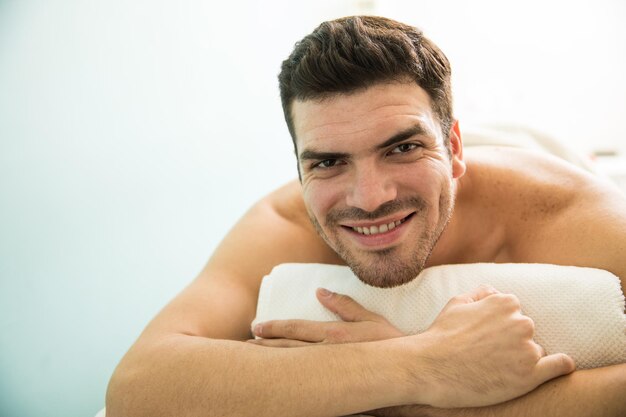 Ritratto di un giovane ispanico attraente sdraiato su un letto in una spa e sorridente
