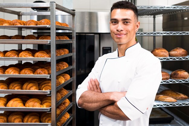 Ritratto di un giovane panettiere fiducioso maschio davanti a scaffali di croissant al forno