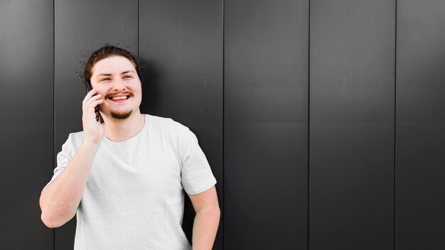 Ritratto di un giovane sorridente parlando al cellulare contro il muro nero