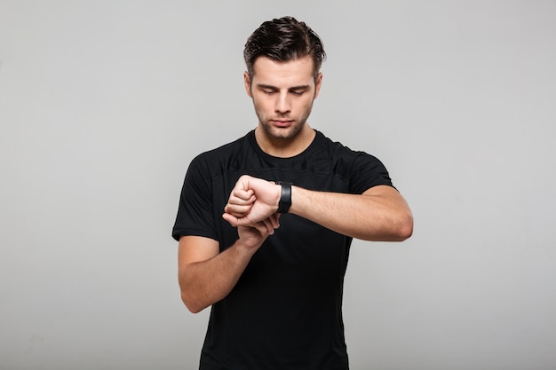 Ritratto di un giovane sportivo concentrato che regola il suo orologio da polso