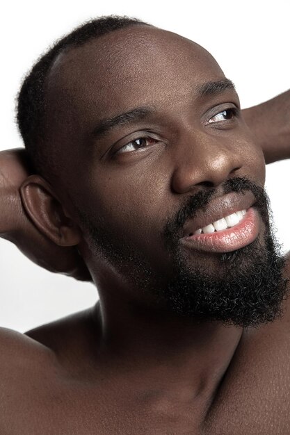 Ritratto di un giovane uomo africano sorridente felice nudo in studio. Modello maschile di alta moda in posa e isolato su sfondo bianco