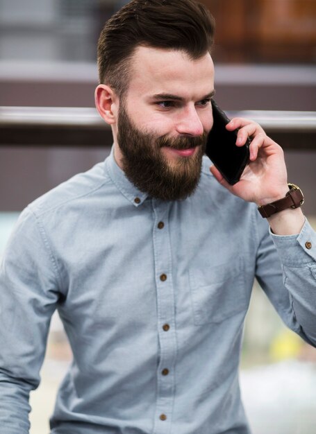 Ritratto di un giovane uomo barbuto sorridente parlando sul cellulare