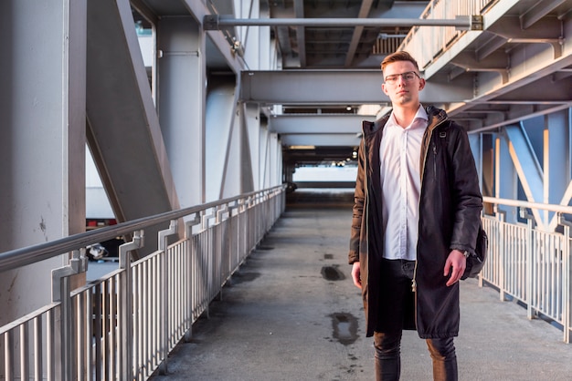 Ritratto di un giovane uomo che indossa giacca lunga in piedi sul ponte