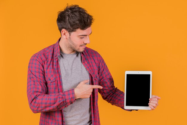 Ritratto di un giovane uomo che punta il dito contro la tavoletta digitale contro uno sfondo arancione