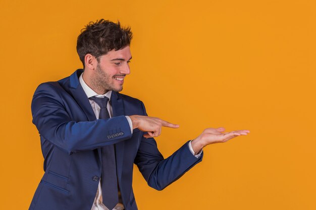 Ritratto di un giovane uomo d&#39;affari che punta il dito contro qualcosa su uno sfondo arancione