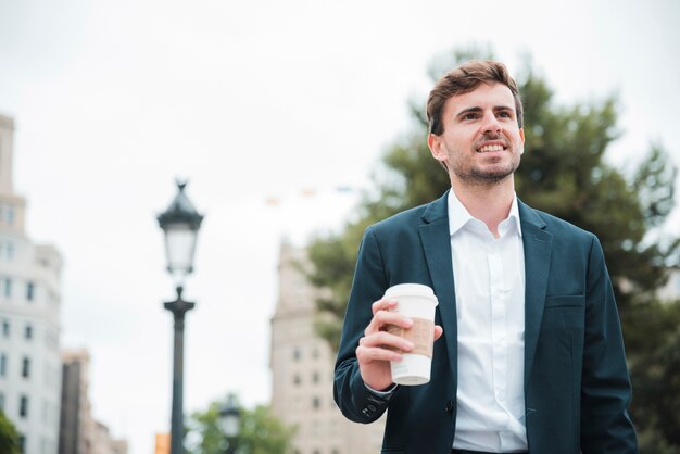 Ritratto di un giovane uomo d&#39;affari sorridente che tiene la tazza di caffè asportabile a disposizione