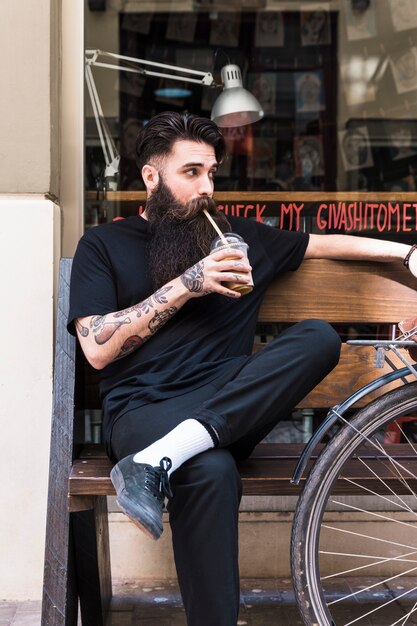 Ritratto di un giovane uomo seduto sulla panchina a bere il delizioso latte al cioccolato rinfrescante