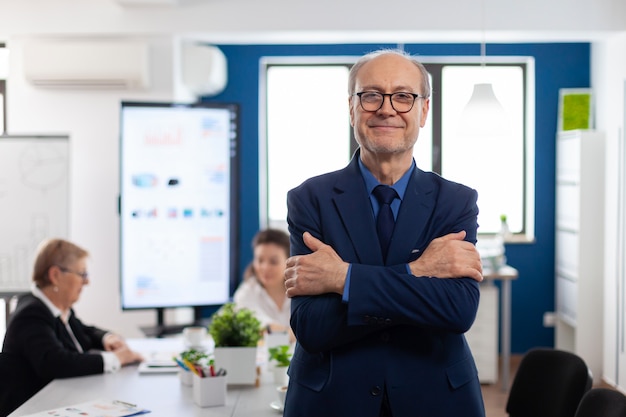 Ritratto di un imprenditore senior di successo nella sala conferenze che sorride alla telecamera con le braccia incrociate