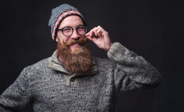 Ritratto di un maschio rosso barbuto con gli occhiali vestito con un maglione di lana e un cappello.