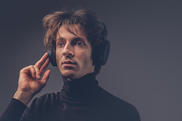 Ritratto di un maschio sensuale creativo in un maglione nero che ascolta musica con le cuffie.