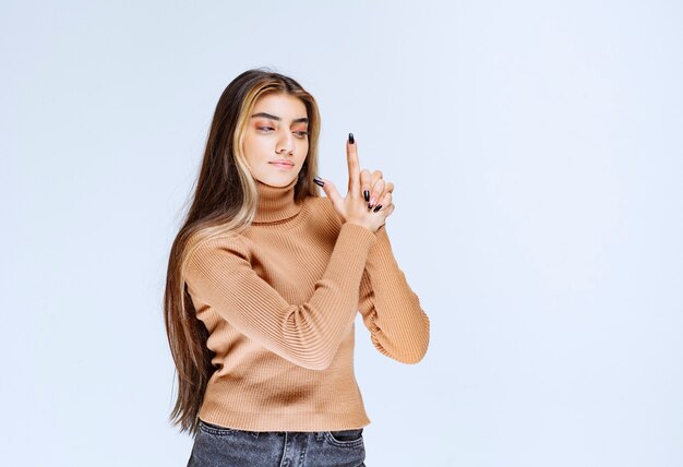 Ritratto di un modello di giovane donna in maglione marrone alzando le dita come una pistola.