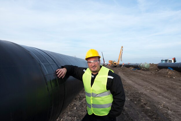 Ritratto di un operaio del giacimento di petrolio in piedi dal tubo del gas al sito in costruzione