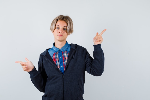 Ritratto di un ragazzo adolescente carino che punta a destra e a sinistra in camicia, felpa con cappuccio e guardando la vista frontale pensierosa