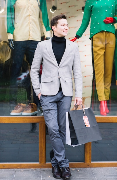 Ritratto di un ragazzo bello che tiene in mano shopping bags in piedi davanti al display della finestra