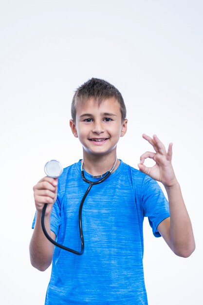 Ritratto di un ragazzo con lo stetoscopio che gesturing segno giusto