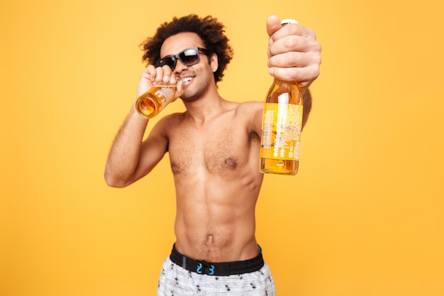 Ritratto di un uomo africano in occhiali da sole che mostra la bottiglia di birra