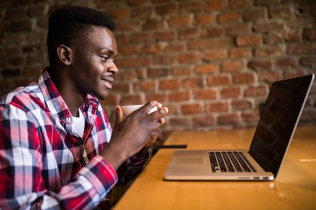 Ritratto di un uomo afroamericano bere caffè e lavorare su un laptop nella caffetteria