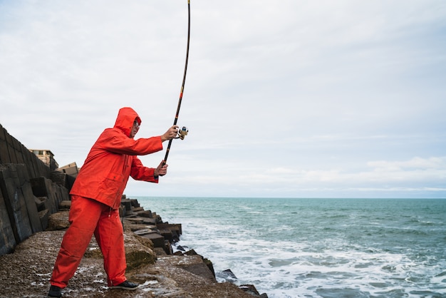 Ritratto di un uomo anziano che pesca sugli scogli al mare. Concetto di pesca.