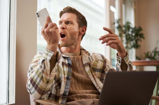 Ritratto di un uomo arrabbiato che urla al suo cellulare un visitatore di un caffè frustrato che discute con qualcuno