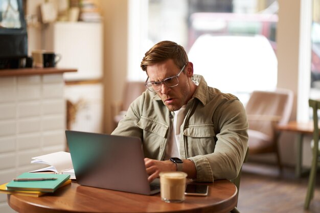 Ritratto di un uomo arrabbiato con gli occhiali che sembra frustrato e che scrive qualcosa sul portatile fissando lo schermo