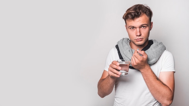 Ritratto di un uomo che prende capsula con acqua su fondo bianco