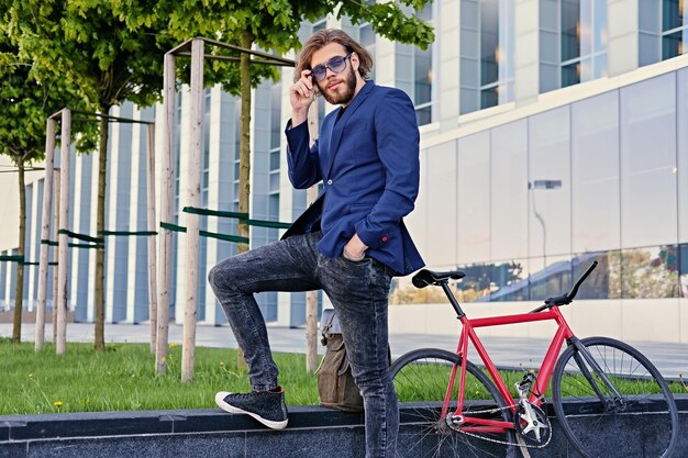 Ritratto di un uomo con lunghi capelli biondi con una bicicletta a velocità singola in un parco cittadino.