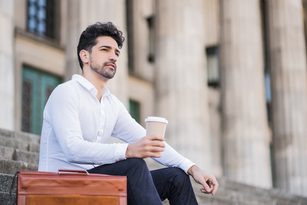 Ritratto di un uomo d'affari che beve una tazza di caffè durante una pausa dal lavoro mentre era seduto sulle scale all'aperto