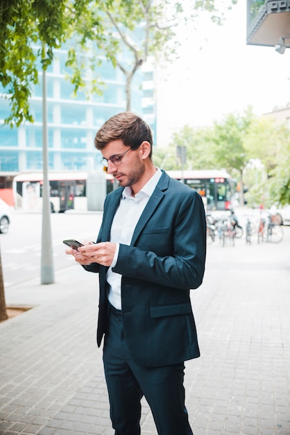 Ritratto di un uomo d&#39;affari in piedi sulla strada utilizzando il telefono cellulare