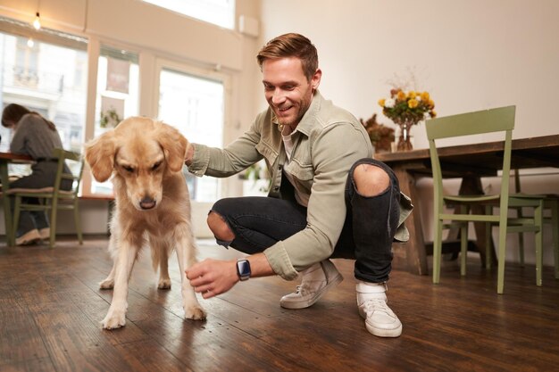 Ritratto di un uomo felice che trascorre del tempo con il suo cane in un caffè adatto agli animali domestici giocando e accarezzando l'oro